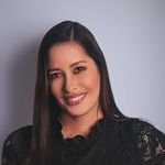 Close-up image of a young woman wearing a black dress, smiling confidently against a light background.